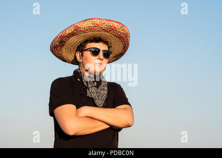 Junge männliche Person im Sombrero und Sonnenbrille im klaren Himmel Hintergrund. Mexiko Unabhängigkeit festliche Konzept der Mann mit nationalen mexikanischen Hut und West Stockfoto