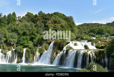 Schöne, klare blaue Wasserfällen durch einen grünen Wald und blauem Himmel umgeben Stockfoto