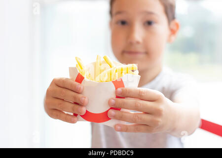 Der Junge 8 Jahre alt hält die Pommes im Plastiketui, Fast food Konzept Stockfoto