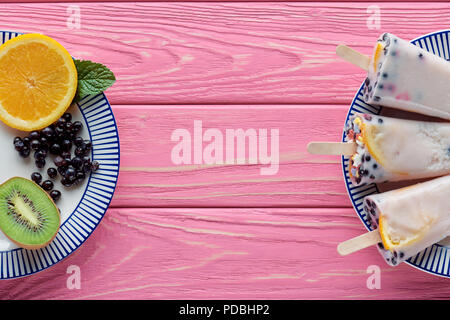 Blick von oben auf die hausgemachte Eis am Stiel und frische Früchte auf Platten auf rosa Holztisch Stockfoto