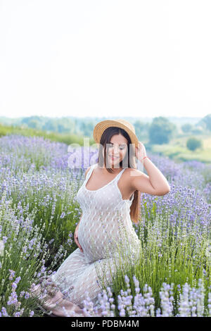 Schöne schwangere Frau in weißem Kleid auf Violett Lavendelfeld posing Stockfoto
