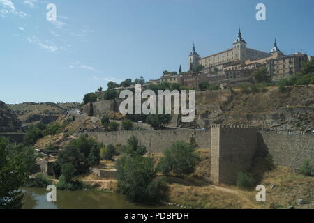 Blick auf den historischen Alcazar in der alten spanischen Stadt Toledo. Die Verteidigungsmauern säumen das Flussufer und das alte Denkmal steht stolz auf dem Hügel. Stockfoto