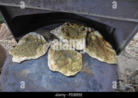 Outdoor Cooking Zubereitung eine flache Brot Pita auf einem saj - eine eiserne Kuppel geformt Pan, das verwendet wird, um das pita Brot auf zu kochen. Es ist mehr als eine Quelle von h platziert Stockfoto