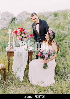 Vertikale Ansicht der Braut auf dem Stuhl, während der Bräutigam in Ihrer Nähe steht. Berge Lage. Stockfoto