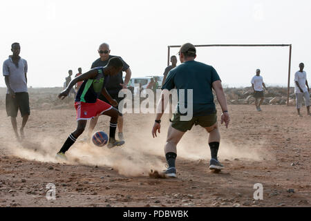 Us-Mitglieder zu Combined Joint Task Force - Horn von Afrika zugeordnet, an einer Partie Fußball mit Kindern aus dem nahe gelegenen Dorf, außerhalb von Chebelley Dorf, Dschibuti, Aug 3, 2018. Über 30 Soldaten und Piloten die sich freiwillig für die Öffentlichkeitsarbeit Veranstaltung von der 404Th zivilen Angelegenheiten Bataillon organisiert. (U.S. Air National Guard Foto von Master Sgt. Sarah Mattison) Stockfoto