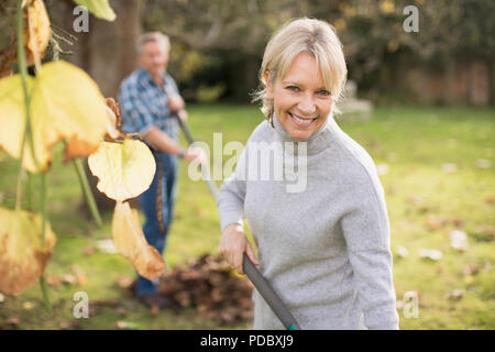 Porträt Lächeln, zuversichtlich, reife Frau harken Blätter im Herbst Hinterhof Stockfoto