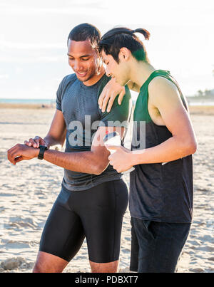 Männliche Läufer ruht, Kontrolle smart Watch fitness Tracker auf Sunny Beach Stockfoto