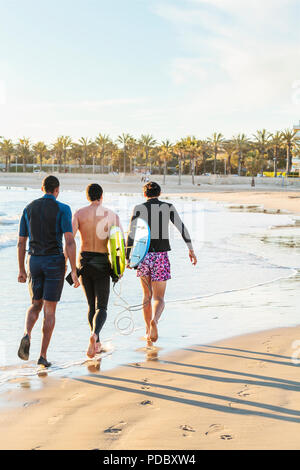 Männliche Surfer gehen mit Surfboards an sonnigen Strand Stockfoto