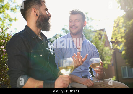 Lächelnd männlichen homosexuellen Paar trinken Weißwein im sonnigen Garten Stockfoto