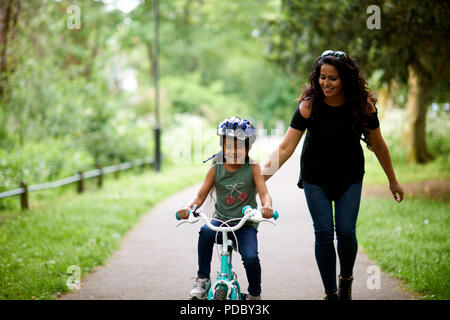 Glückliche Mutter lehre Tochter wie Fahrrad fahren Stockfoto