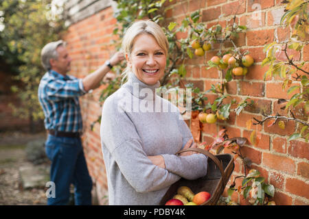 Porträt Lächeln, zuversichtlich, reife Frau ernten Äpfel im Garten Stockfoto