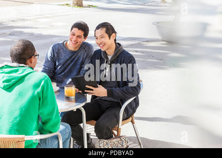 Lächelnd männliche Freunde sprechen am sonnigen Straßencafé Stockfoto