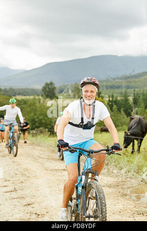 Lächelnd, zuversichtlich reifer Mann Mountainbiken auf ländlichen dirt road Stockfoto