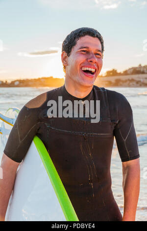 Lachende männliche Surfer mit Surfbrett am Strand. Stockfoto