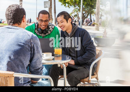 Männliche Freunde mit Laptop am sonnigen Straßencafé Stockfoto