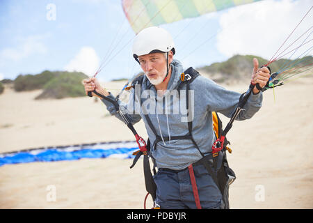 Reife männliche Gleitschirm mit Ausrüstung und Fallschirm am Strand konzentriert Stockfoto