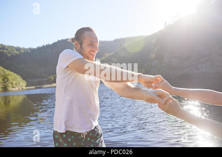 Verspieltes Paar Hände halten am sonnigen Sommer See Stockfoto