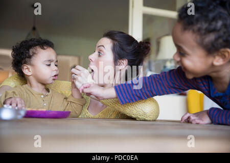 Verspielte Mutter feeding baby Sohn am Tisch Stockfoto