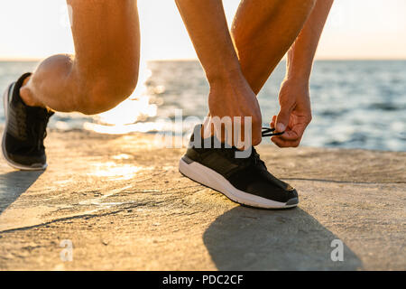 7/8 Schuß von Sportler schnüren Sneakers an Küste vor Sonnenaufgang Stockfoto