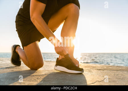 7/8 Schuß von Sportler schnüren Sneakers an Küste vor Sonnenaufgang Stockfoto