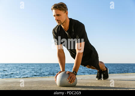 Athletische erwachsener Mann tun Push-ups mit Fit Ball auf Meer Stockfoto