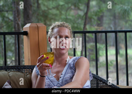 Hübsche blonde Dame, entspannen Sie auf der Terrasse, ein Glas Wein zu trinken, auf der Suche nach oben. Model Released Stockfoto