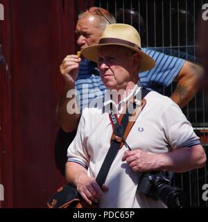 Ältere Fotograf in einem Sonnenhut bei Sidmouth Folk Festival, in der geschäftigen Innenstadt. East Devon, Großbritannien. August, 2018. Stockfoto