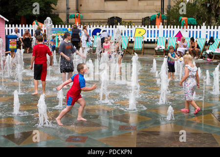 In einem Sheffield Park in Yorkshire spielen Kinder in Wasserstrahlbrunnen. Wetter in Großbritannien. An einem heißen Sommertag, an dem fröhliche Kinder in den kühlen interaktiven Brunnen spielen, ist es ein warmer, heller Tag für eine sommerliche Abkühlung im städtischen Brunnen. Stockfoto