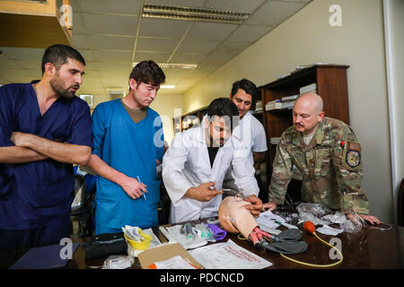 Der PROVINZ KANDAHAR, Afghanistan (5. August 2018) - U.S. Navy Leutnant Cdr. Travis J. Fitzpatrick, leitende Krankenschwester für Kandahar Airfield Rolle der NATO III Multinationale medizinische Einheit, beobachtet, wie Afghanischen Medizinischen Mitarbeiter demonstrieren, wie eine Fluglinie zu öffnen, 5. August 2018, während einer medizinischen Beratung Besuch bei Kandahar regionale militärische Krankenhaus, Camp Held in Kandahar, Afghanistan. Mitarbeiter aus der Rolle III Durchführung Routinemäßige Besuche auf KRMH zu trainieren und afghanischen medizinischen Personal beraten. (U.S. Armee Foto: Staff Sgt. Neysa Canfield/TAAC-Public Affairs) Stockfoto