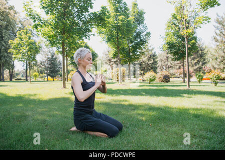 Frau Yoga und Geste mit den Händen auf Gras im Park Stockfoto