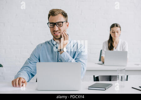 Junge Unternehmer in Brillen Leiden von Zahn Schmerzen während im Büro arbeiten Stockfoto