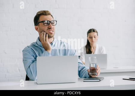 Junge Unternehmer leiden unter Zahnschmerzen und Holding Glas Wasser am Arbeitsplatz Stockfoto