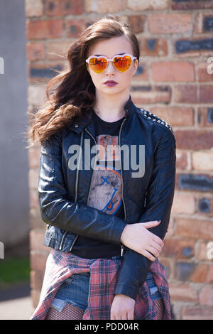 Eine alternative suchen Mädchen stehend außerhalb trägt ein Biker Jacke, mit einer Mauer im Hintergrund. Stockfoto