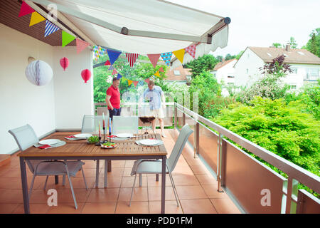 Gerne Freunde Spaß haben und ihre Reden und trinkt Bier beim Grillen von Fleisch und Gemüse auf Terrasse Stockfoto