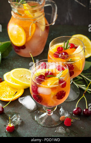 Selbstgemachte erfrischende Wein Sangria oder Lochen mit Früchten in Gläsern. Sangria Cocktails mit frischem Obst, Beeren und Rosmarin. Auf einen Stein oder Schiefer hinterg Stockfoto
