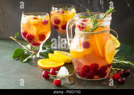 Selbstgemachte erfrischende Wein Sangria oder Lochen mit Früchten in Gläsern. Sangria Cocktails mit frischem Obst, Beeren und Rosmarin. Auf einen Stein oder Schiefer hinterg Stockfoto