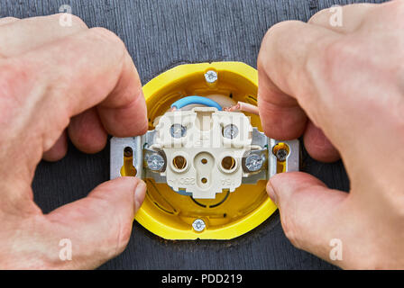 Die Strompreise für die privaten Haushalte, der Elektriker ist der Einbau einer internen Teil des Haushalts steckdose in gelbe Wand, close-up. Stockfoto