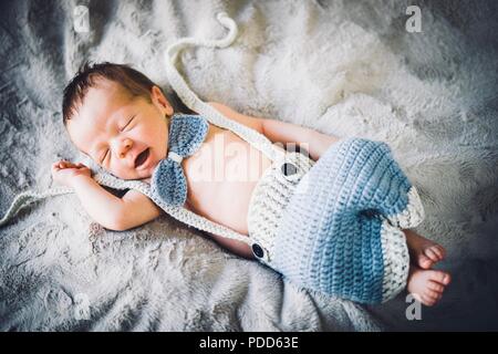 Ein neugeborenes Baby schlafen in Blau und Grau Fliege und Hosen aus Gewirken Stockfoto