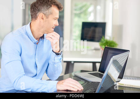Schuss kalkulierender Geschäftsmann vor dem Laptop sitzen und nachdenklich bei Arbeiten auf Neues Projekt. Stockfoto