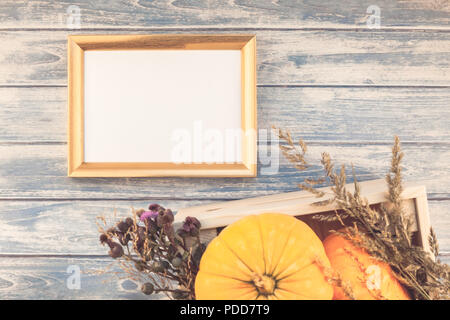 Blick von oben auf die Herbst orange Kürbisse und trockene Blumen mit Gras Danksagung Hintergrund in blau getönten Holztisch mit goldenen Rahmen mock up und Kopieren Stockfoto