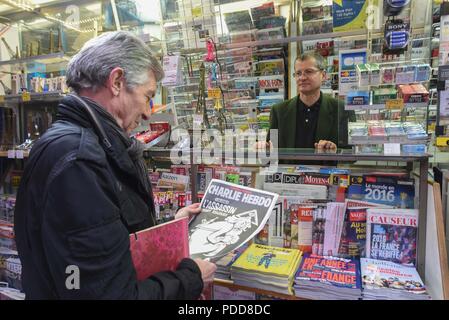 Januar 6, 2016 - Paris, Frankreich: Portrait von Ray CospŽrec, der gerade die neueste Ausgabe von Charlie Hebdo gekauft mit einem mörderischen monotheistischen Gott auf dem Deckblatt. Im Hintergrund, Patrick Morault, die Zeitungen verkauft, sagt, daß er erwartet, zehn Mal mehr Kopien von Charlie Hebdo als üblich zu verkaufen. Gedenken de l'Sprengstoffanschlag contre Charlie Hebdo, un ein Apres l'attaque. *** Frankreich/KEINE VERKÄUFE IN DEN FRANZÖSISCHEN MEDIEN *** Stockfoto