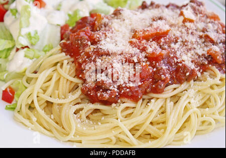 Gekochte spaghetti Pasta gekrönt mit einem köstlichen hausgemachten Soße und frisch geriebenem Parmesan und einem frischen Garten Salat garniert mit cremig Stockfoto