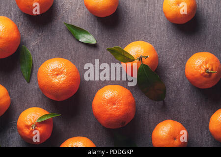 Oben Blick auf saftige orange Mandarinen mit grünen Blättern ist die Verlegung auf vintage Holztisch. Stockfoto