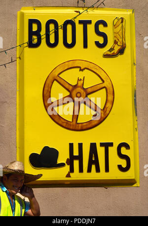 Ein ungelernter Arbeiter Gespräche über sein Smartphone neben einem Store verkaufen Western Boots und Cowboy Hüte in Santa Fe, New Mexico. Stockfoto