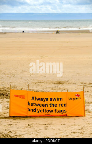 Große gelbe RNLI Water safety banner Menschen Beratung zwischen dem roten und gelben Flaggen zu schwimmen. Stockfoto