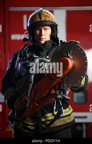 Foto von Ernst Feuerwehrmann mit Kettensäge tragen Helm auf dem Hintergrund der Fire Engine Stockfoto