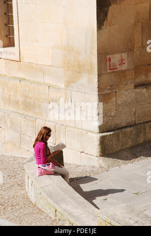 Frau mit einem Buch sitzen auf Steinbank. Santo Domingo de Silos, Burgos, Spanien. Stockfoto