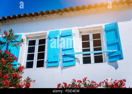 Traditionelle weiße griechische Weiß mit blauen Fensterläden in Mediterraneanstyle und rosa Blüten. Fiskardo, Kefalonia, Griechenland Stockfoto