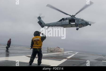 Gewässer südlich von Japan (14. Mai 2018) der Luftfahrt Bootsmann Mate (Handling) 1. Klasse Thinh Dai begrüsst einem MH-60S Sea Hawk, zugeordnet zu den militärischen Sealift Command (MSC) Dry Cargo/Munition ship USNS Cesar Chavez (T-AKE 14), nach der Vermittlung der Sprengkörper auf dem Flugdeck an Bord der Marine vorwärts - bereitgestellt Flugzeugträger USS Ronald Reagan (CVN 76), als Teil einer Auffüllung-auf-See während der Probefahrt. Die nicht-Kämpfer, zivil-Crewed Charter Schiff, vom MSC betrieben, Benzin, Essen, Kampfmittel, Ersatzteile, Mail und andere Verbrauchsmaterialien zur Marine Schiffen in der ganzen Welt. Ronald Reagan, das Flaggschiff der Auto Stockfoto