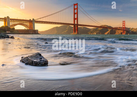 Lange Belichtung eines atemberaubenden Sonnenuntergang am Strand durch die berühmte Golden Gate Bridge in San Francisco, Kalifornien Stockfoto